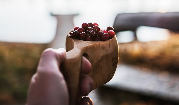Mies pitää kädessään puista kuksaa, joka on täynnä punaisia marjoja.