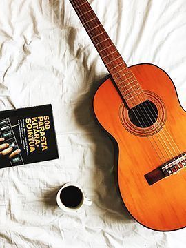 Kitara, soitto-opas ja kahvikuppi lakanan päällä