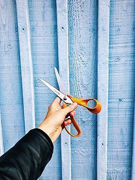 Sakset kädess talon seinä taustalla