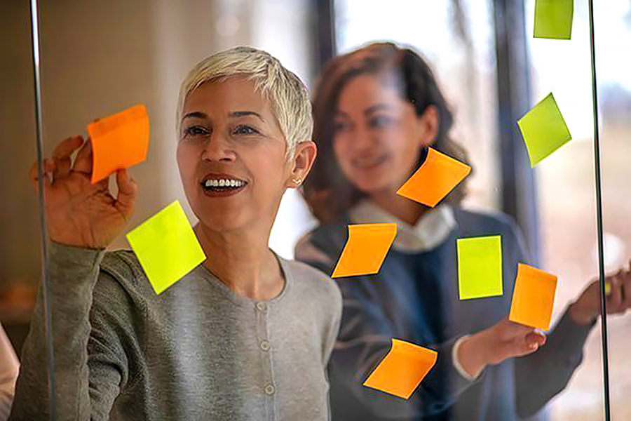 Kaksi naista kirjoittaa lasiseinään liimatuille muistilapuille