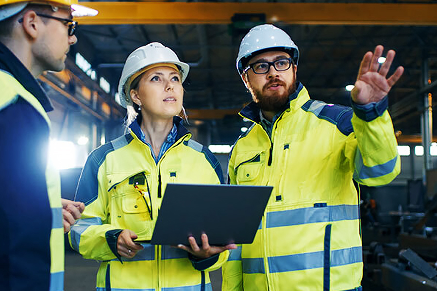 Kaksi työasuista miestä ja yksi nainen työpalaverissa varastossa